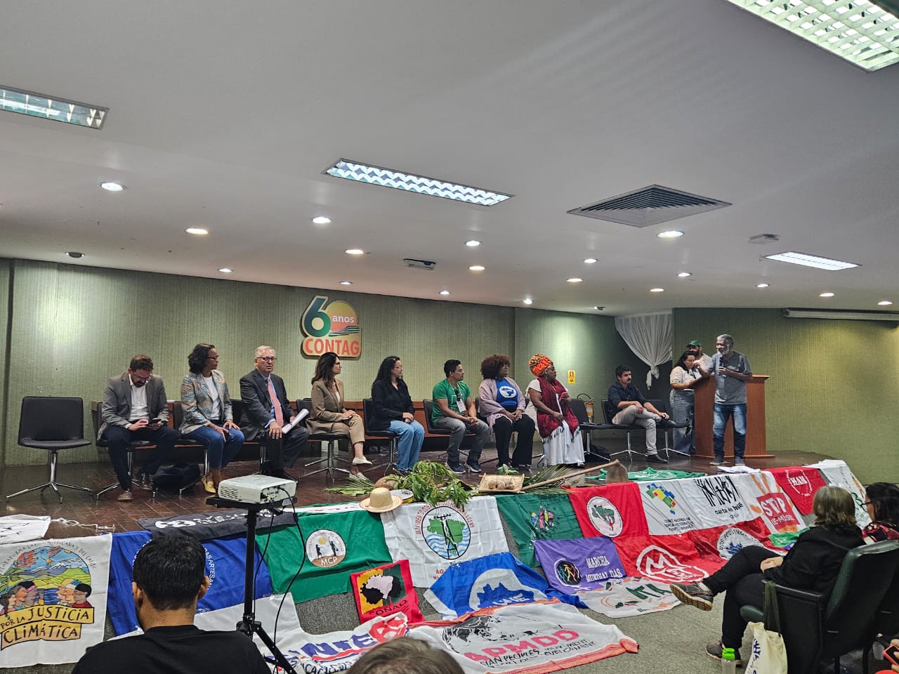 Palco com representantes do governo e ao chão diversas bandeiras dos movimentos sociais